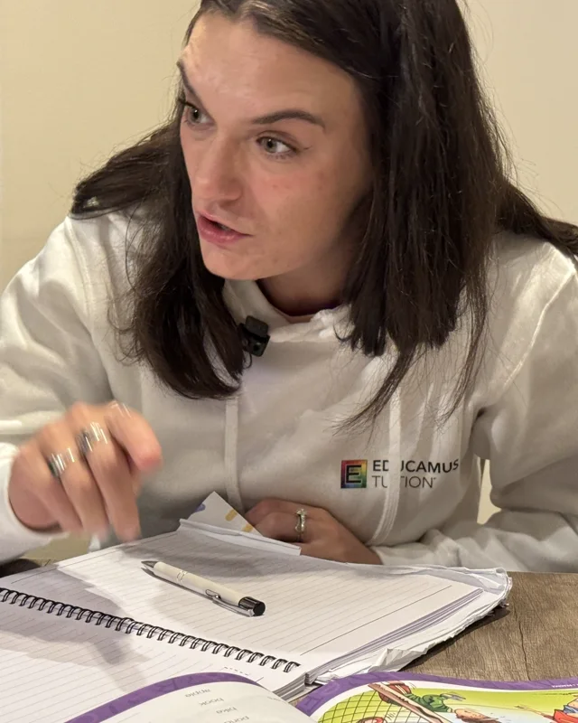 Olivia, an Educamus Tuition English tutor, teaching with a workbook and notepad in an Educamus Tuition hoodie